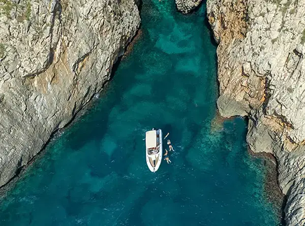 Boat surrounded by rocky cliffs and swimmers